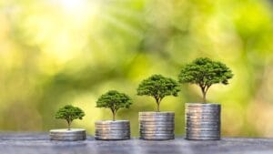 Image of four stacks of coins with growing trees, symbolizing Overcoming Mental Blocks and financial growth, set against a blurred green background.