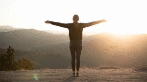 Anxiety: Woman with arms outstretched in a power pose, facing a sunrise over mountains.
