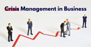 A conceptual image titled "Crisis Management in Business" featuring four small figurines of businessmen in suits positioned along a jagged red graph line on a white background. The graph ascends and descends dramatically, symbolizing volatility. The first figure stands solitary at the graph’s peak, while the next two interact closely as the line dips, suggesting collaboration during downturns. The final figure stands confidently at the graph’s recovery point. The composition visually represents navigating business crises through adaptability and teamwork.