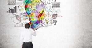 Creative professional sketching a vibrant, multicolored light bulb on a concrete wall, symbolizing innovation and strategic thinking. The bulb radiates splashes of rainbow hues and contains smaller icons like a brain, rocket, and dollar signs, surrounded by diagrams of graphs, charts, and startup-related terms (e.g., 'Success,' 'Idea,' 'Startup'). The artist, dressed in a white shirt and black pants, holds a paintbrush, actively adding details to the mural. The scene blends artistic expression with business concepts, emphasizing the fusion of creativity and analytical planning in achieving goals.