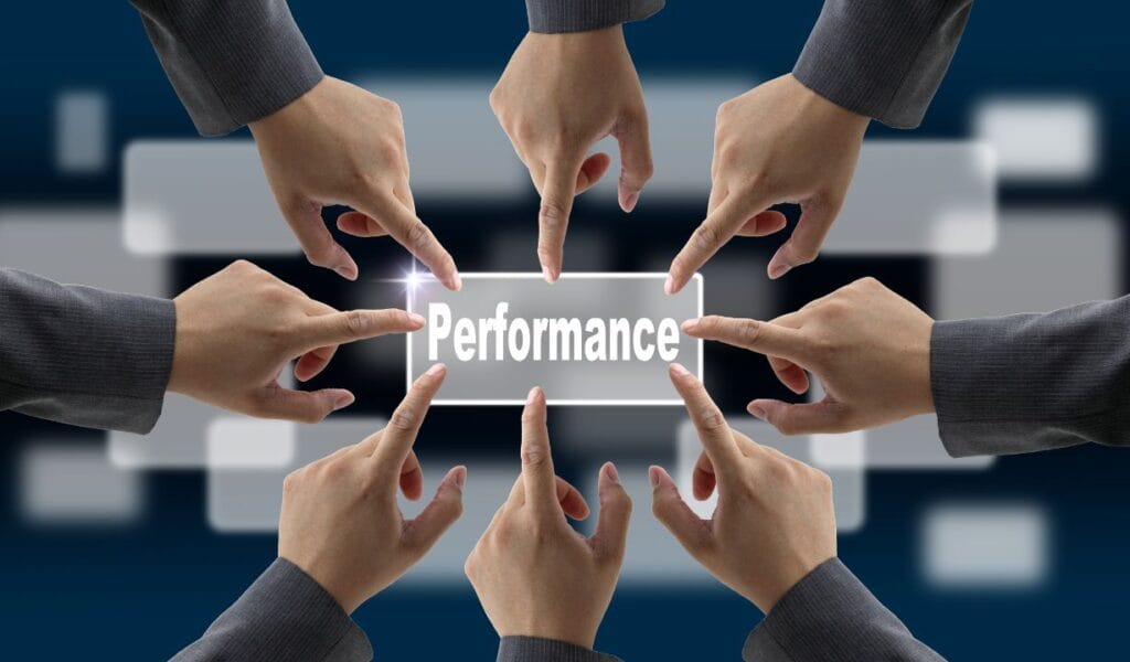 An illustration showing multiple hands pointing toward a glowing, transparent rectangular sign with the word 'Performance' written on it. The hands are reaching from different directions, symbolizing collaboration and collective focus on achieving performance goals. The background is dark and blurred, featuring abstract geometric shapes that suggest a professional or corporate setting. The overall design emphasizes teamwork and shared responsibility in driving performance.