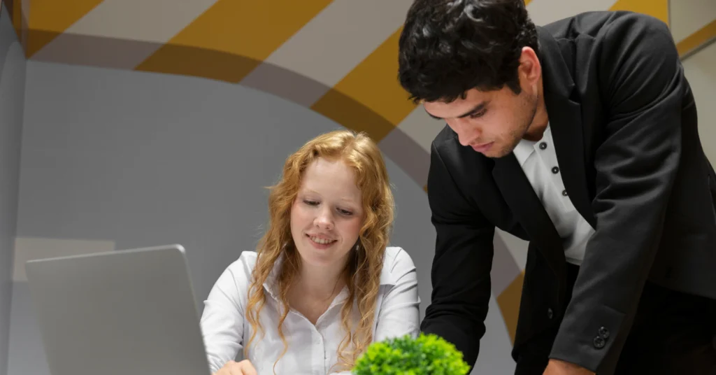 Two people collaborating at a laptop with a plant.