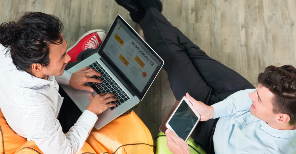 Two people on beanbags, one with a laptop, one with a tablet.