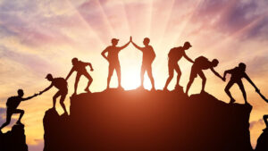 Silhouettes of people helping each other on a mountain during sunset, symbolizing teamwork in Leadership Retreats.