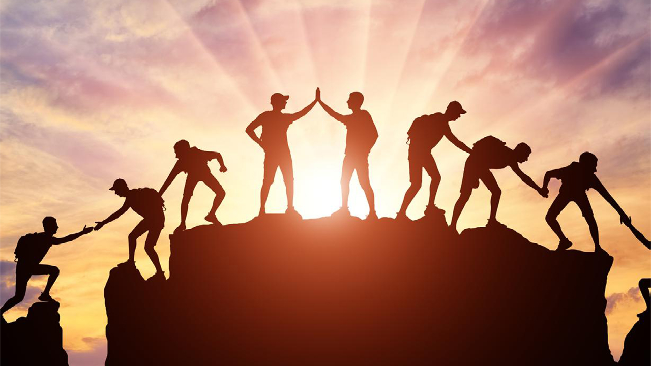 Silhouettes of people helping each other on a mountain during sunset, symbolizing teamwork in Leadership Retreats.
