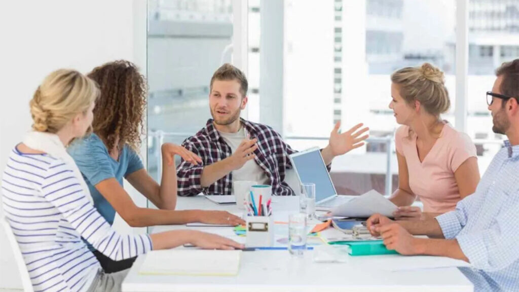 Mastering Sales with NLP: Five professionals discuss strategies in a modern office with laptops and documents.