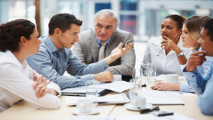 Group meeting for Coaching Business with professionals discussing around a table with laptops, papers, and coffee cups.