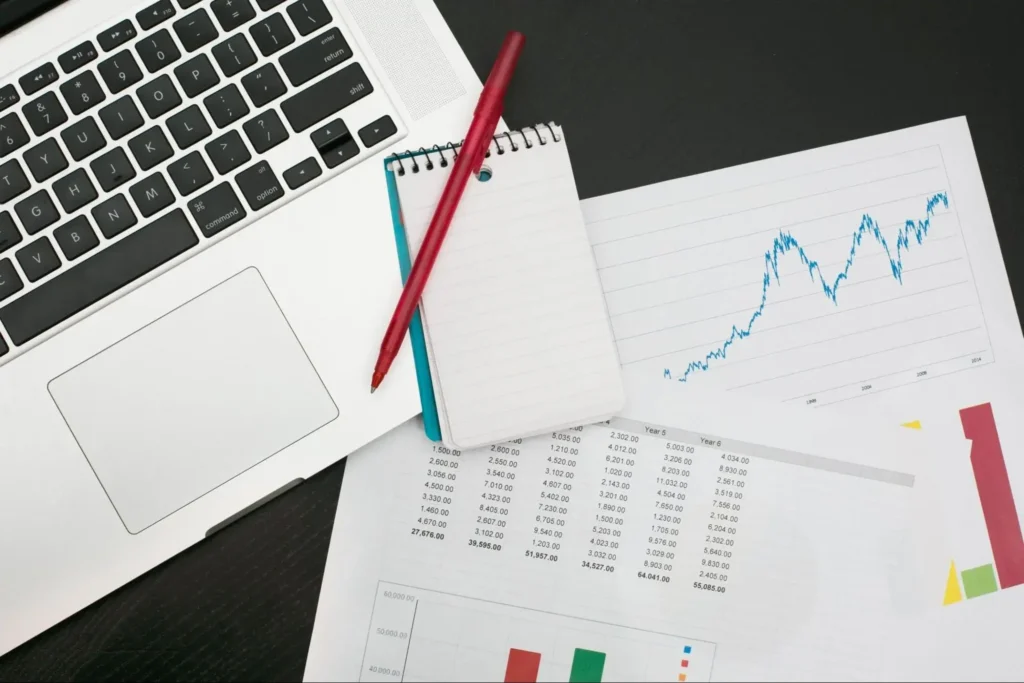 Laptop with financial charts, notebook, and pen representing business planning and growth strategy